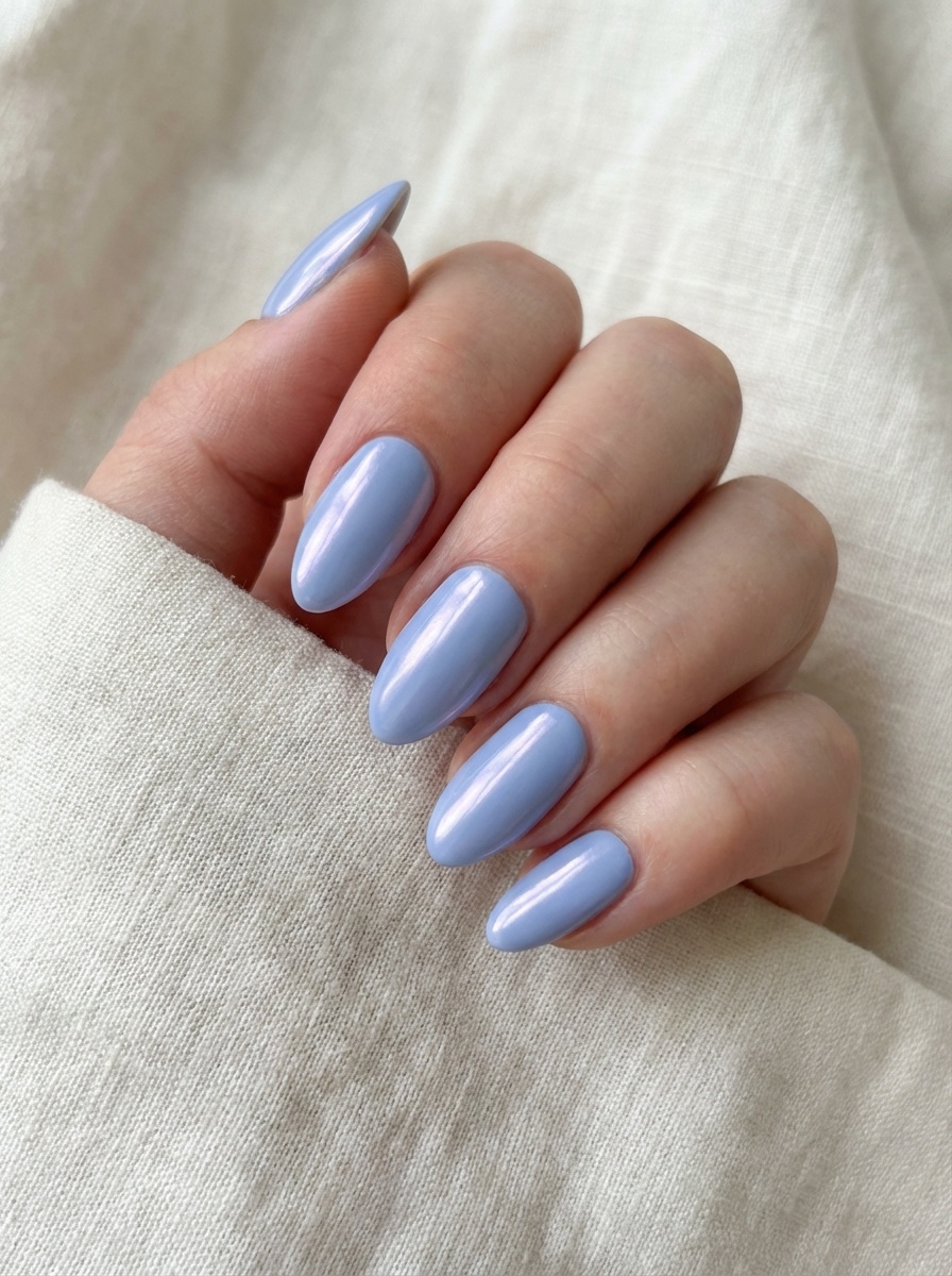 A hand partially wrapped in beige fabric, featuring a blue almond nail art idea with almond-shaped nails finished in a glossy, light periwinkle-blue shade.