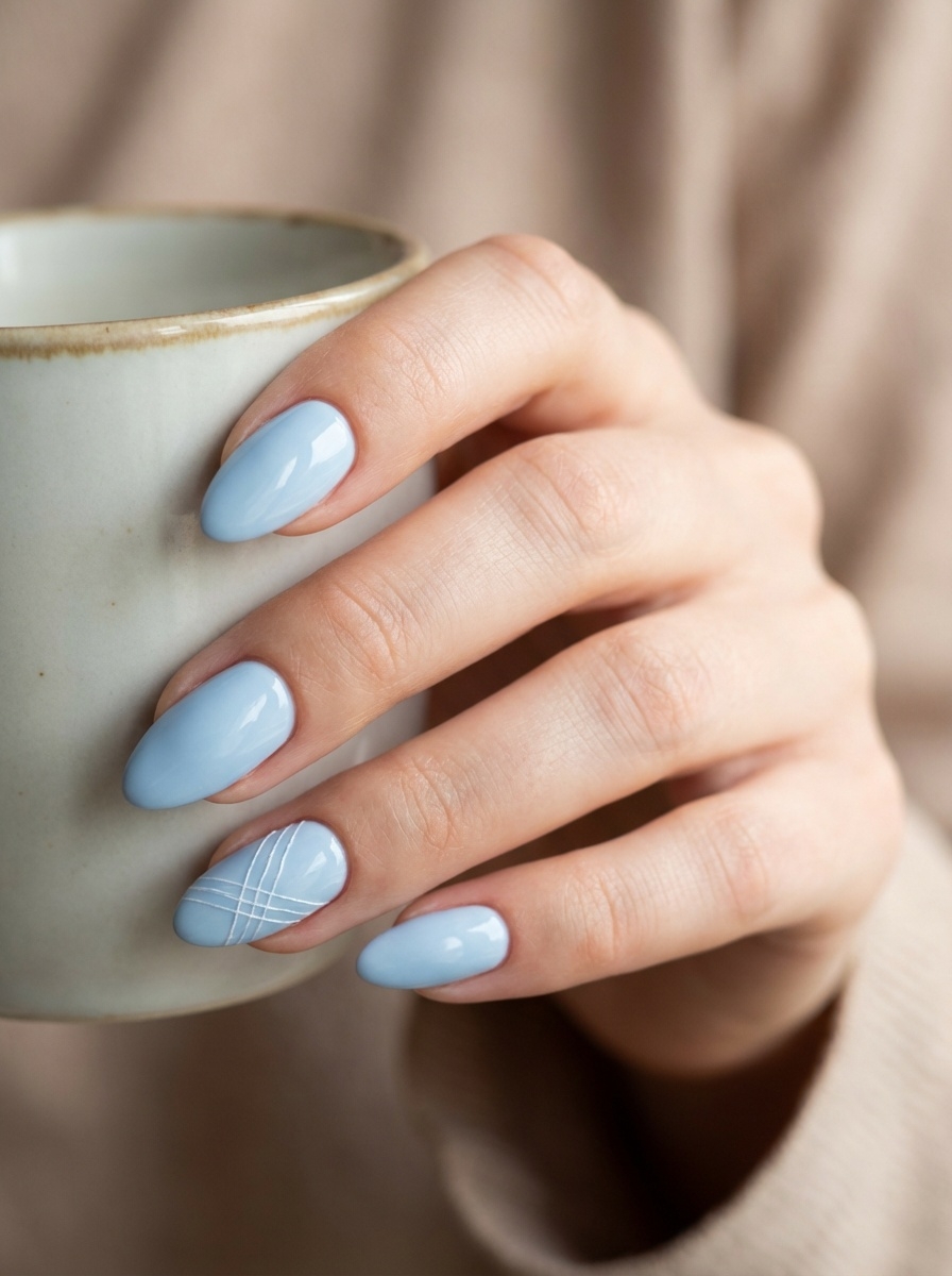 A relaxed hand holding a neutral-toned mug, featuring a blue almond nail art idea with pastel blue almond nails and a subtle white line accent nail.