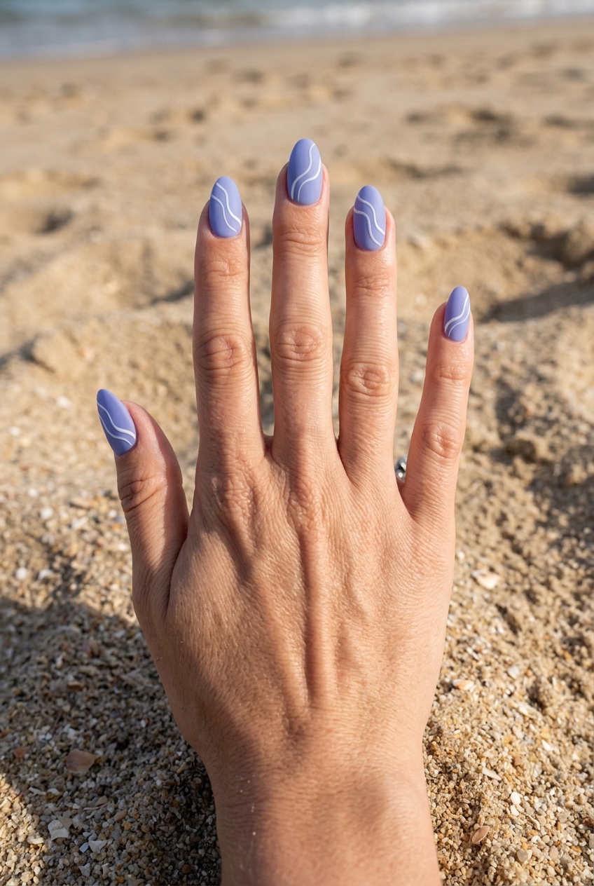 A hand placed on sandy beach ground showing a matte purple nail art idea with periwinkle matte nails and delicate white wave line designs on each nail