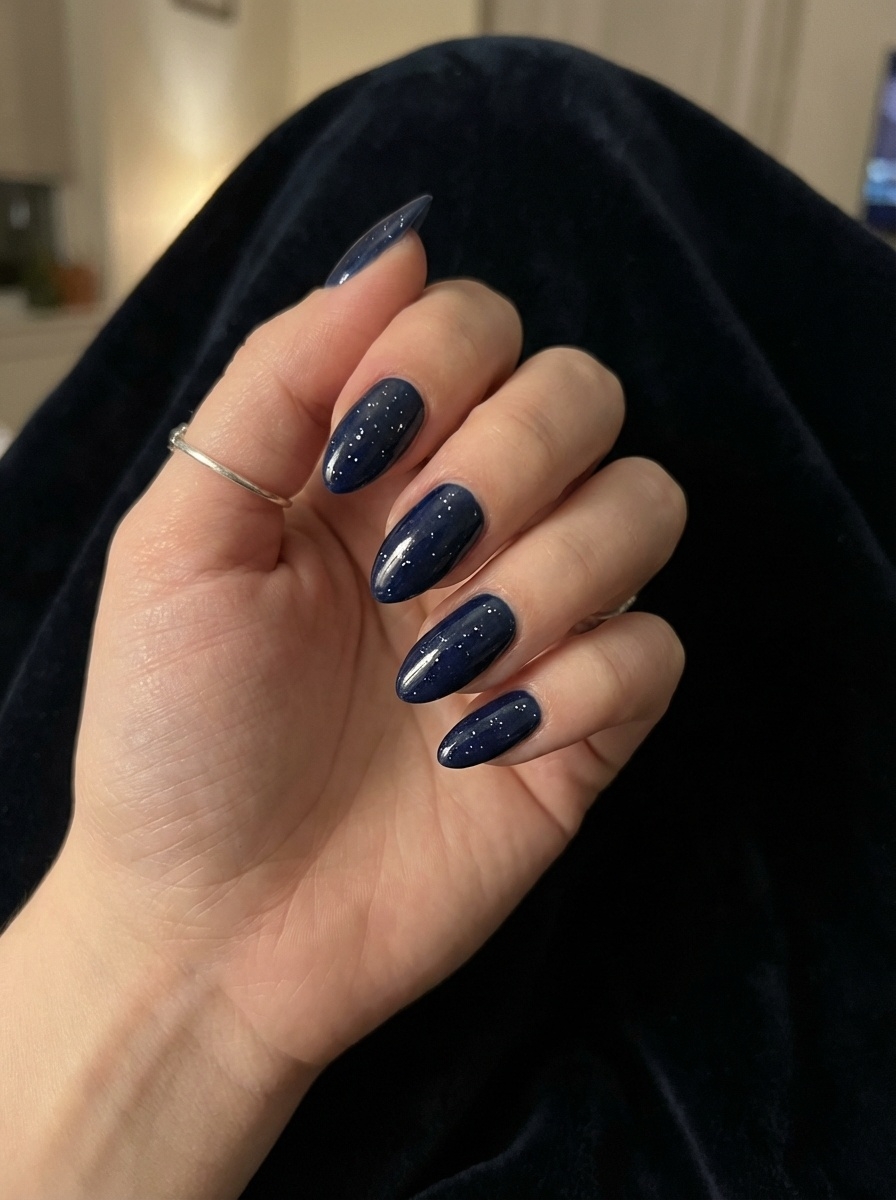 Close-up of a hand with a blue almond nail art idea, showcasing deep navy almond nails with fine shimmer details and a high-gloss finish.