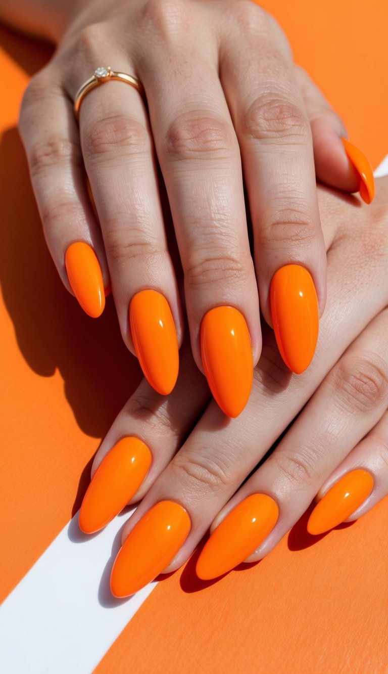 Close-up of two hands with long almond-shaped nails in bright neon orange polish against an orange background, showcasing a bold orange almond nail art idea with a glossy finish