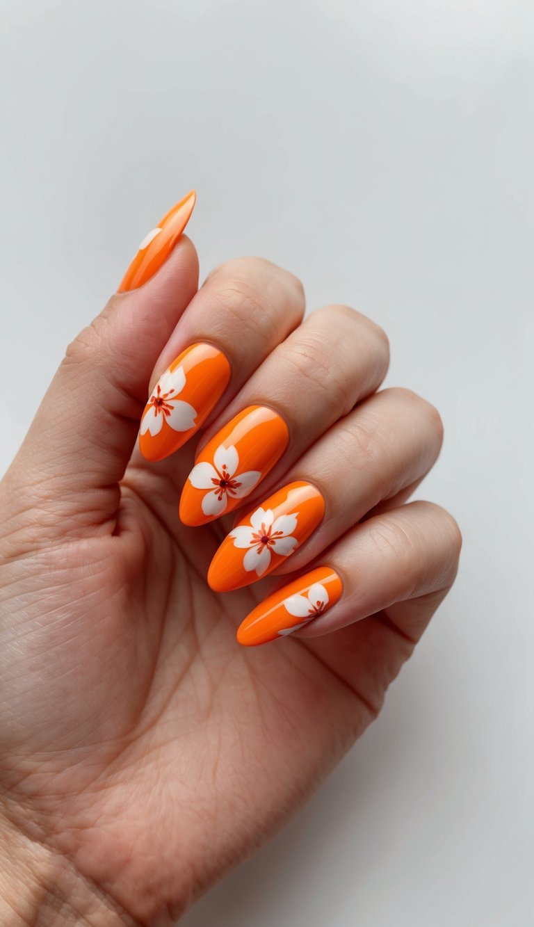 Close-up of a hand with almond-shaped nails in vivid orange, highlighting an orange almond nail art idea with a detailed citrus fruit design and fine leaf patterns on accent nails
