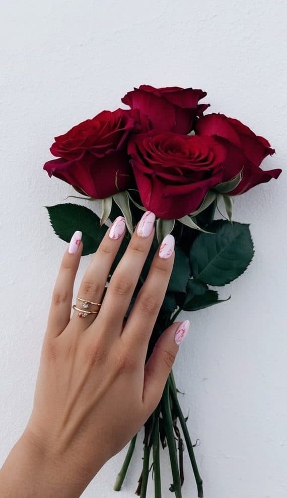 A hand with pink marble-designed nails holding a bouquet of red roses on a white background