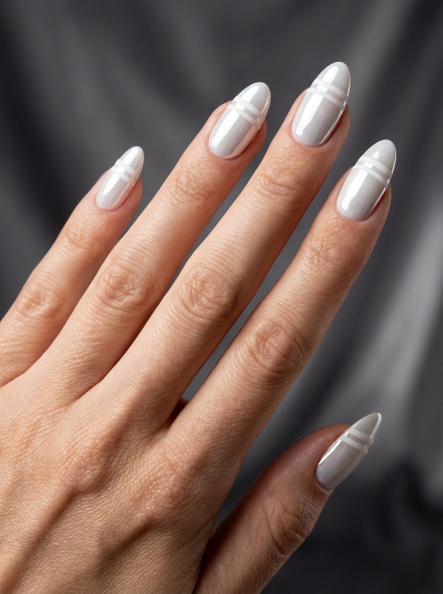 Hand extended against a dark fabric backdrop, featuring a white chrome nail art idea with almond-shaped pearl chrome nails and thin horizontal white stripe detailing.