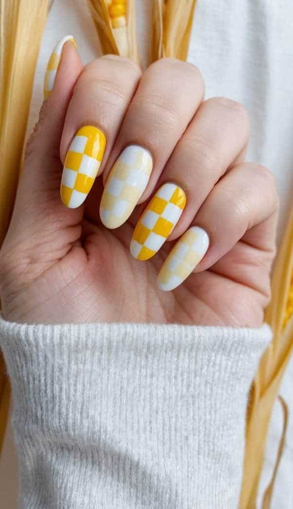 A close-up of cheerful yellow and white checkerboard nail art on a cornsilk background