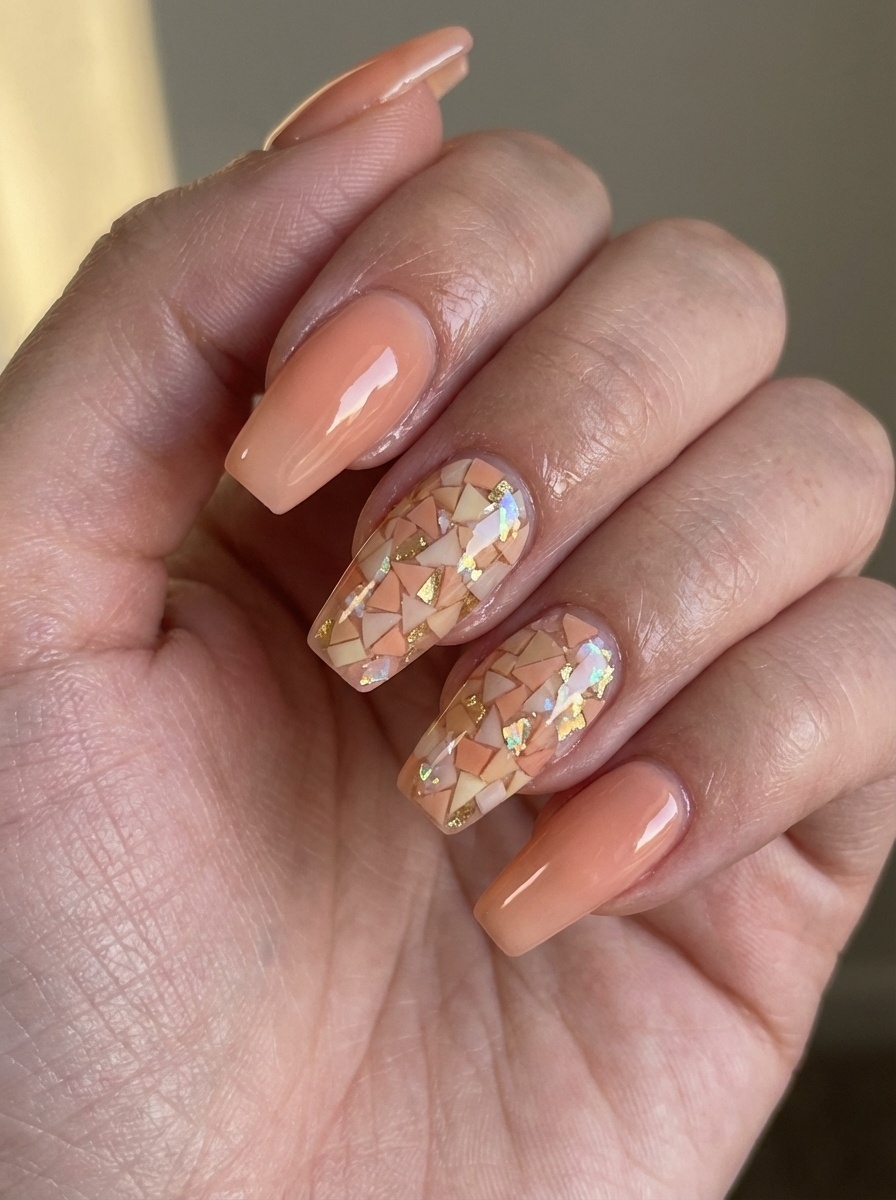 A close-up of manicured nails with a soft peach base, where two feature nails display intricate mosaic-like fragments in cream, coral, and gold—mirroring a stained-glass peach nail art idea.