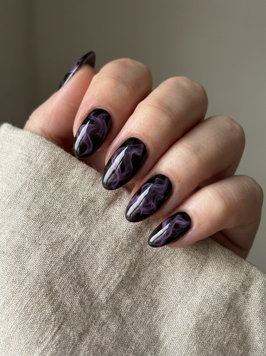 Resting against neutral fabric, fingers reveal shiny black nails with translucent purple smoke patterns drifting across the surface, highlighting a purple and black nail art idea.