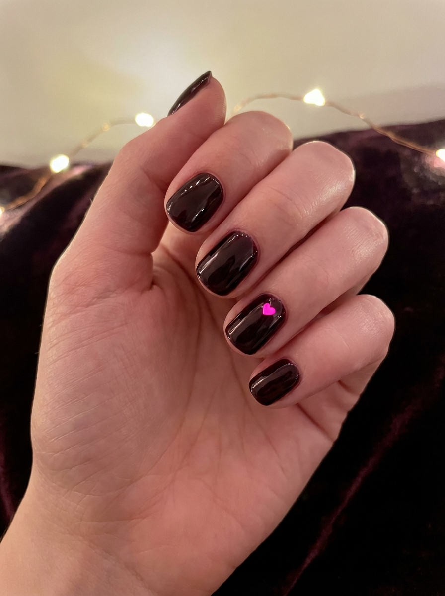 Angled view of a hand showing glossy black nails with a single pink heart accent on one finger, styled as minimalist valentine's nail art ideas.