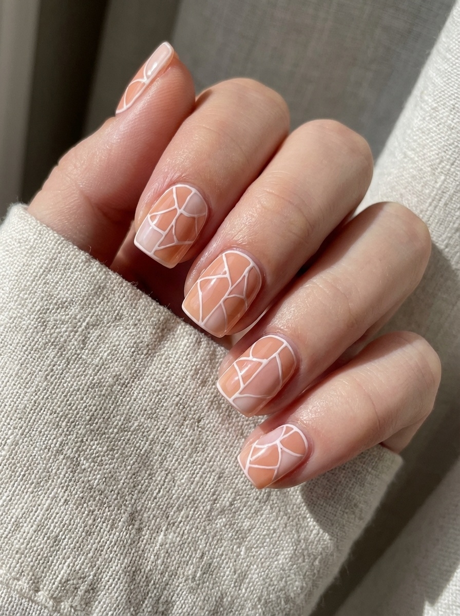 A cozy hand in a cream sleeve showing peach-toned nails with soft matte finishes and white abstract linework—evoking a serene and structured peach nail art idea.