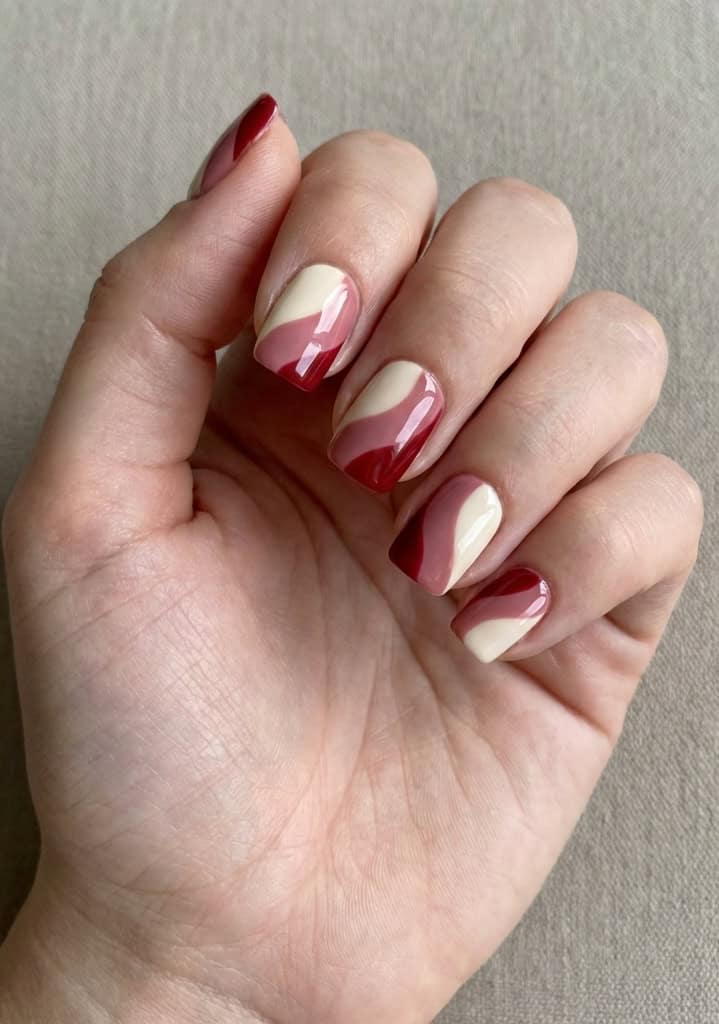 Fingers gently curled on textured fabric, highlighting glossy nude nails with sweeping red and blush swirl designs, styled as artistic valentine's nail art ideas.