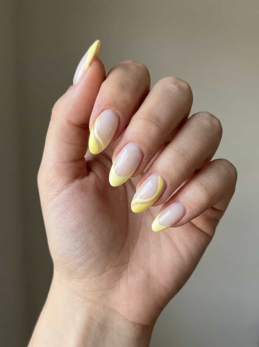 Hand with a yellow nail art idea showing sheer nails accented by pale yellow French tips and wavy stripe details, giving a minimalist manicure a dynamic edge.