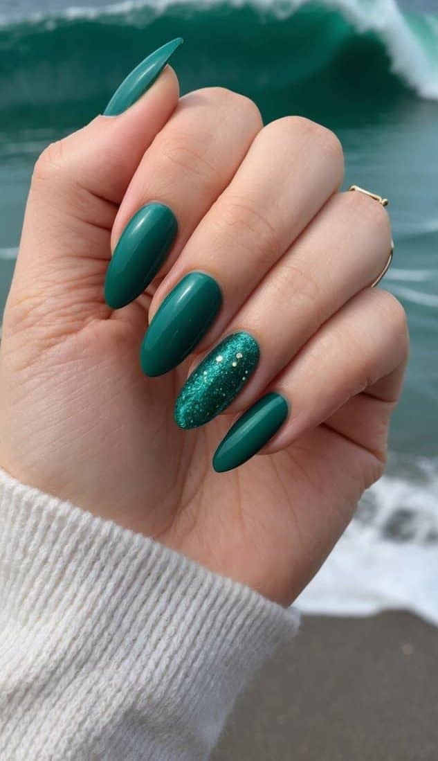 A close-up view of green almond-shaped nails against a backdrop of emerald waves crashing on the shore