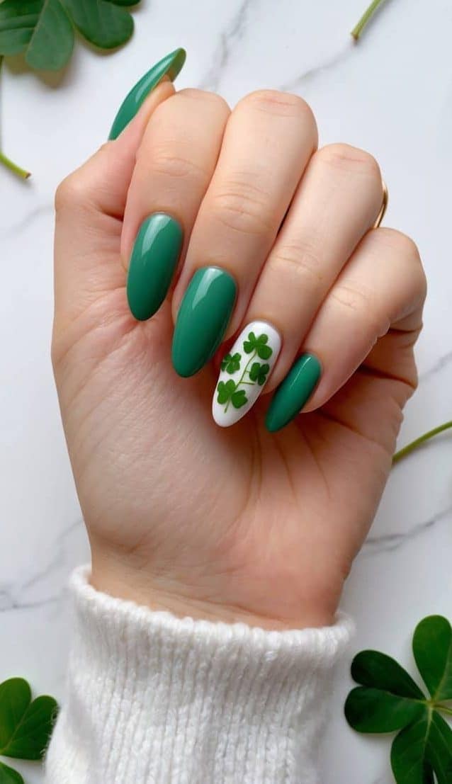 Fresh green almond nails arranged on a white marble background with clover and ivy accents