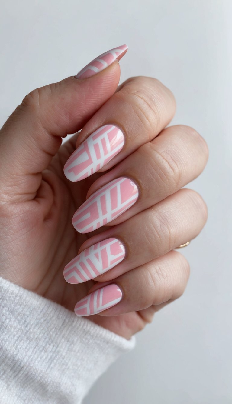 Hand with elongated pastel pink nails designed with clean white angular lines for a soft yet structured look, highlighting a pink and white nail art idea