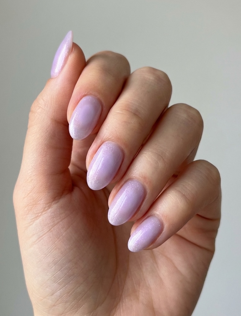 Hand with almond-shaped nails showcasing a lavender nail art idea in soft shimmer and pale lavender polish for a romantic, subtle finish.