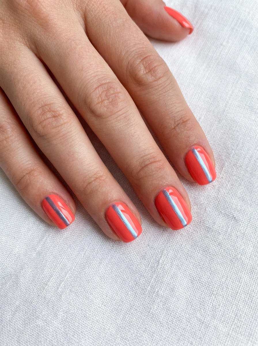 Hand with short coral nails featuring vertical metallic silver stripes—this bold spring break nail art idea is clean, edgy, and perfect for warmer days.