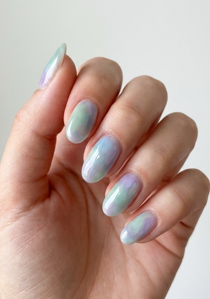 Close-up of a hand with long, glossy nails in watercolor swirls of purple, green, and blue—an ethereal spring break nail art idea with soft edges.