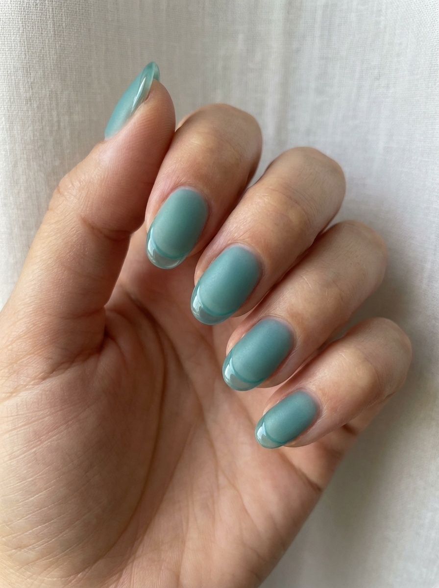 Hand resting against sheer fabric showing a teal nail art idea with short rounded nails painted in a muted sea-glass teal shade with a soft satin sheen.