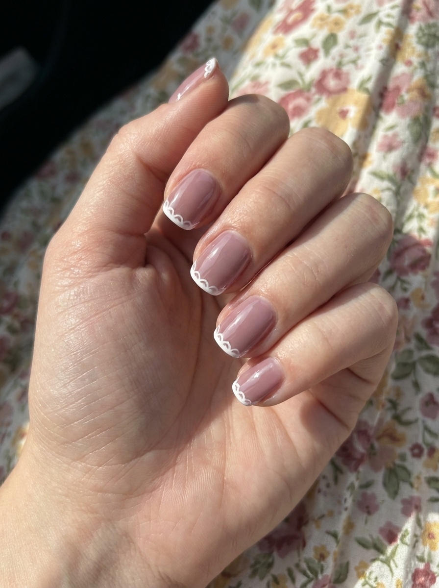 A close-up of a hand in sunlight highlights a mauve nail art idea with sheer mauve polish and delicate lace-style white edging on each nail.