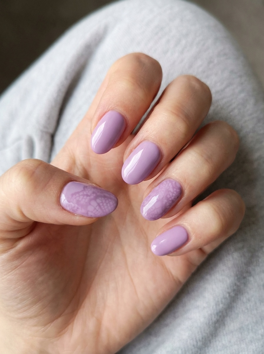 Against a soft gray background, a hand displays a lilac nail art idea with rounded lavender nails and a single accent nail showing a subtle cloudy marble effect.