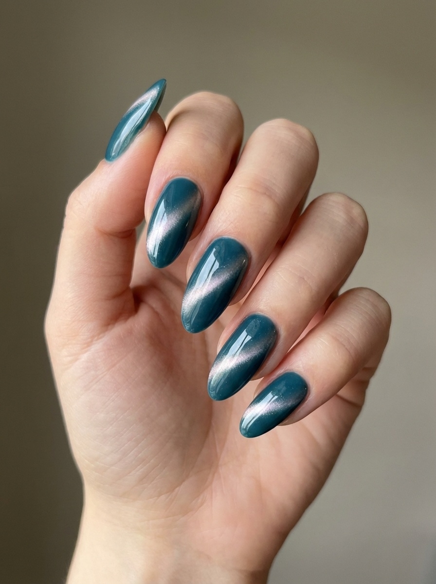 An angled view of a hand showcases a teal nail art idea with metallic teal almond nails, reflecting light smoothly across each curved surface.