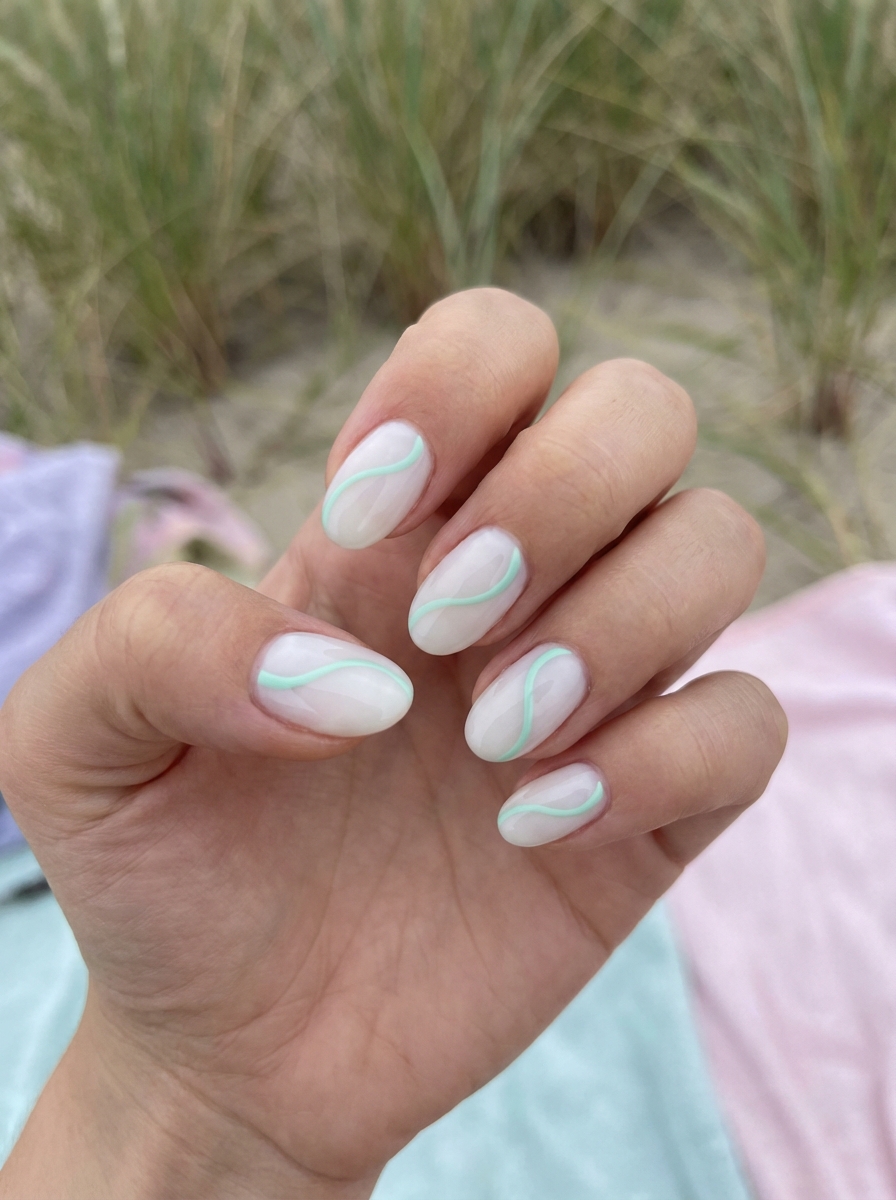 Natural light highlights a mint green nail art idea on short almond nails, showing sheer nude polish layered with thin mint green flowing lines against a soft outdoor background.
