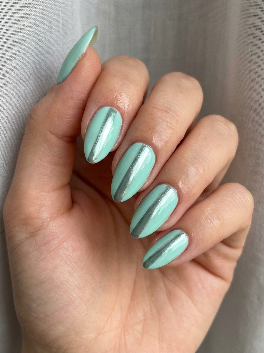 Soft indoor lighting highlights a mint green nail art idea with glossy mint almond nails, each finished with a centered metallic chrome stripe for a refined look.