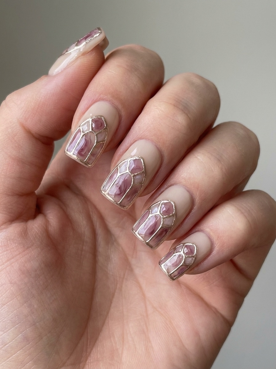 A close-up hand shows a mauve nail art idea with nude nails framed by gold geometric lines and filled with muted mauve sections in a stained-glass style.