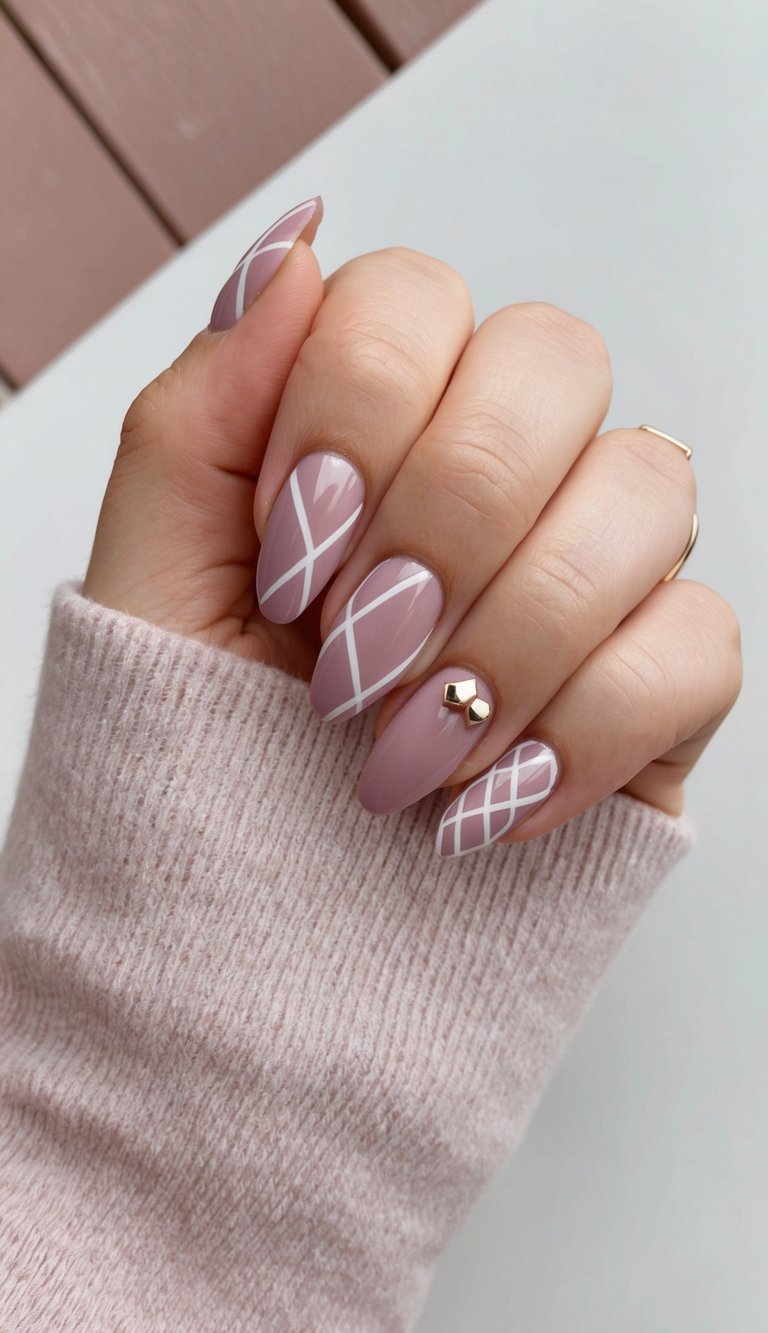 An up-close hand photograph captures a mauve nail art idea with almond-shaped nails, white geometric crisscross patterns, and a minimal gold embellishment.