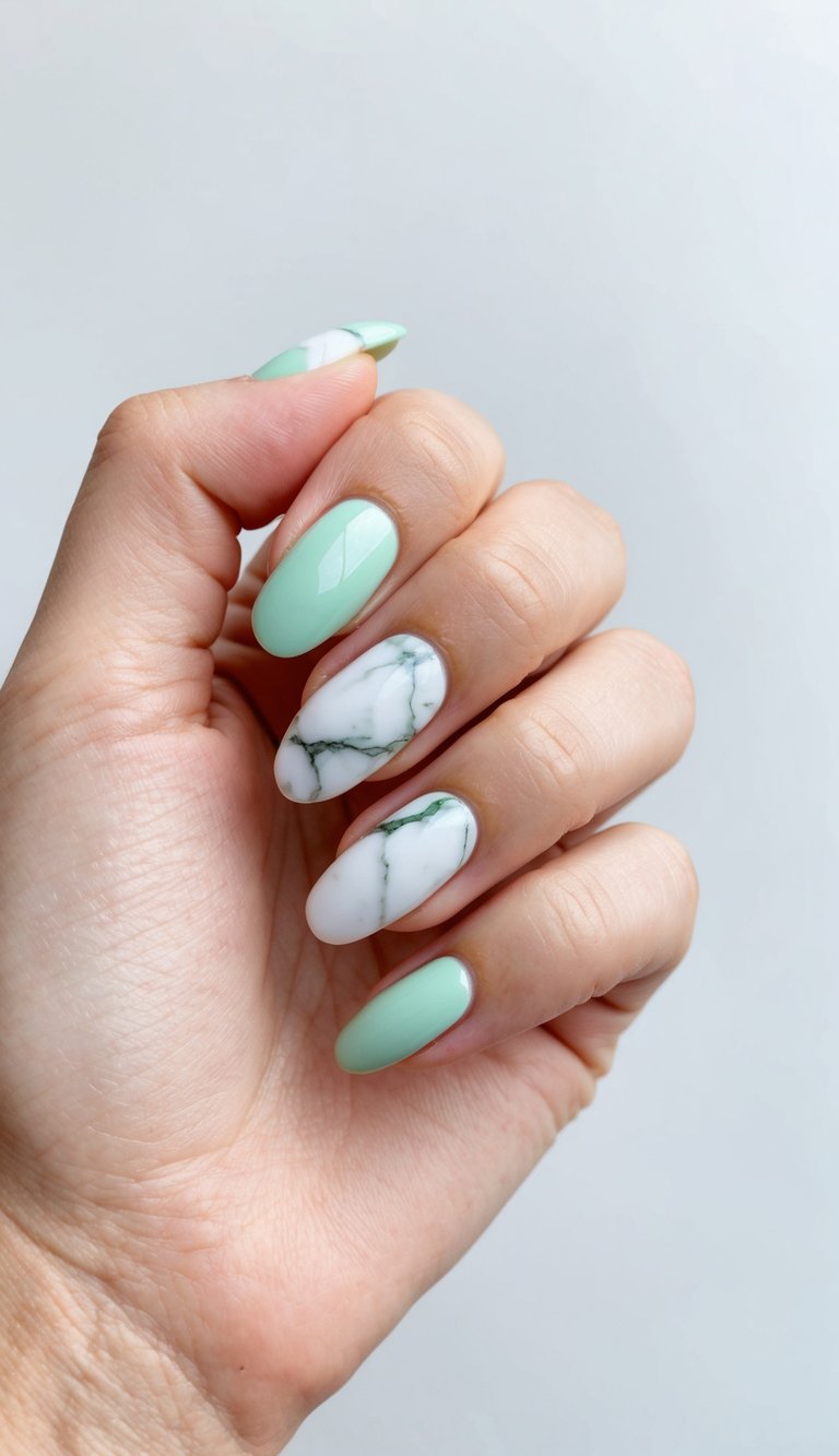 A close-up of a hand with mint green nails paired with white marble accent nails, showing subtle gray veining and a smooth glossy finish against a pale background.