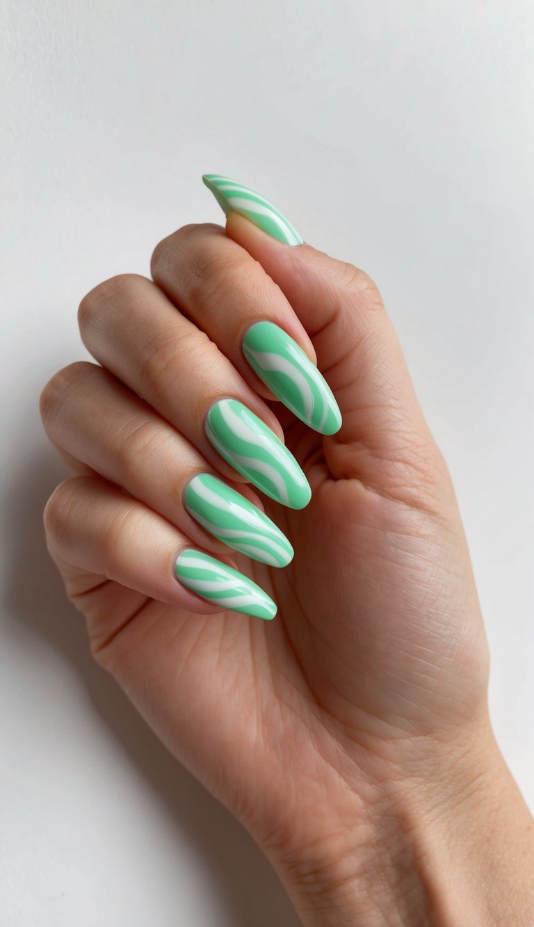 A hand with long, almond-shaped nails painted in a mint green color with white wavy patterns.