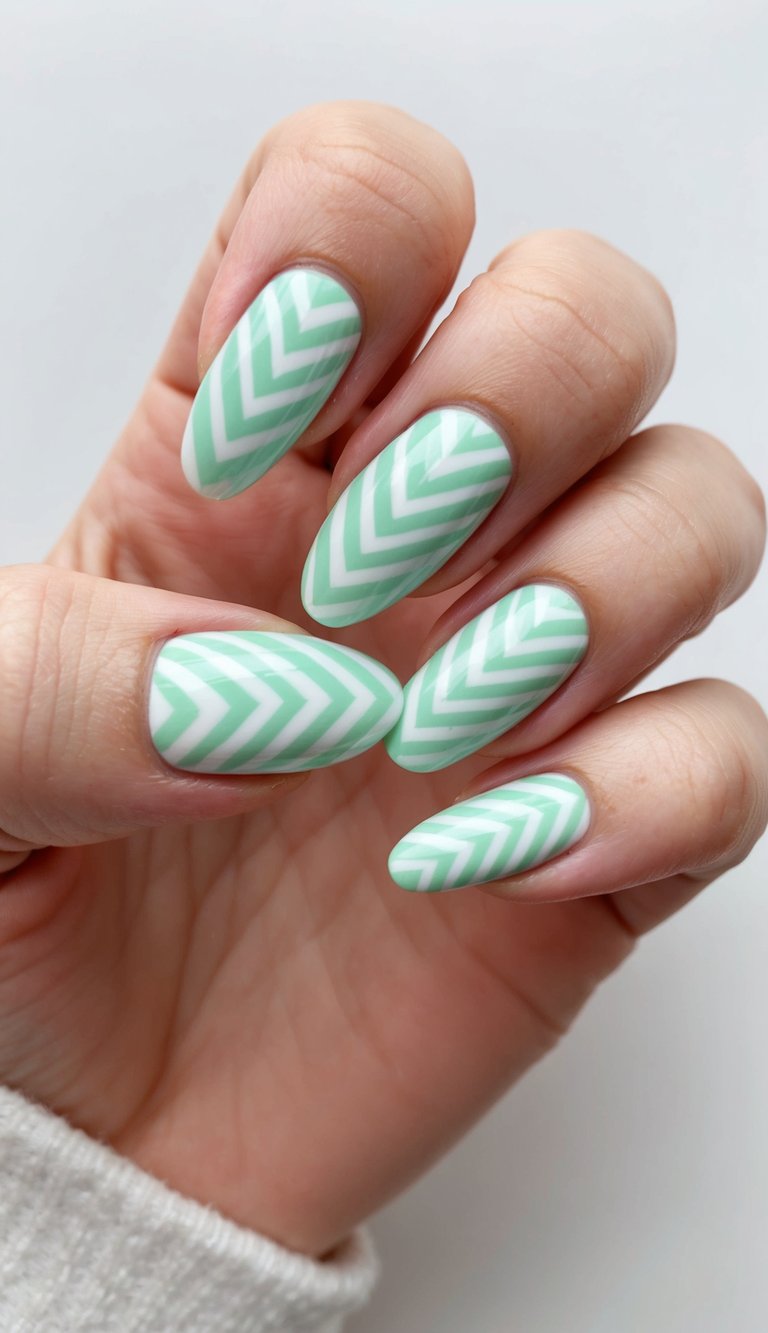 Natural light frames a mint green nail art idea on elongated nails, showing pastel mint tones accented by uniform white chevron striping across all fingers.