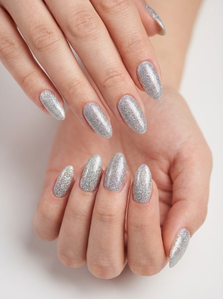 Hands with silver glittery nail polish on stiletto-shaped nails, placed against a light background.