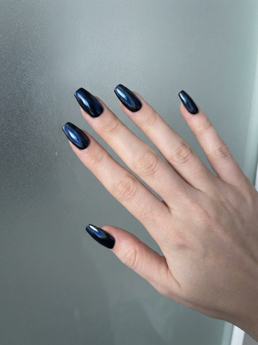 Fingers extended against a smooth gray backdrop revealing a black and blue nail art idea with glossy black nails reflecting a metallic blue chrome glow.