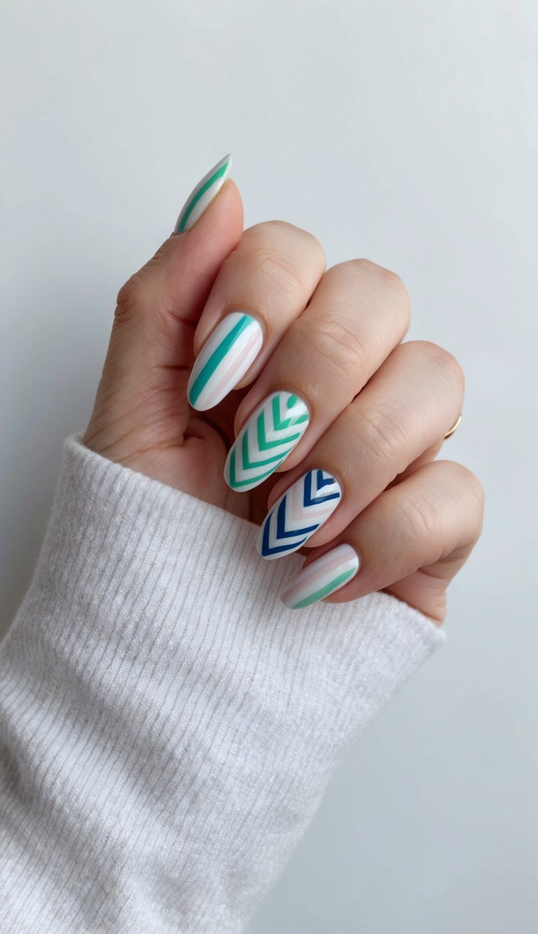 Natural hand wearing a white sleeve presenting a short nail art idea with white base polish and bold teal and navy geometric chevron patterns on short nails.