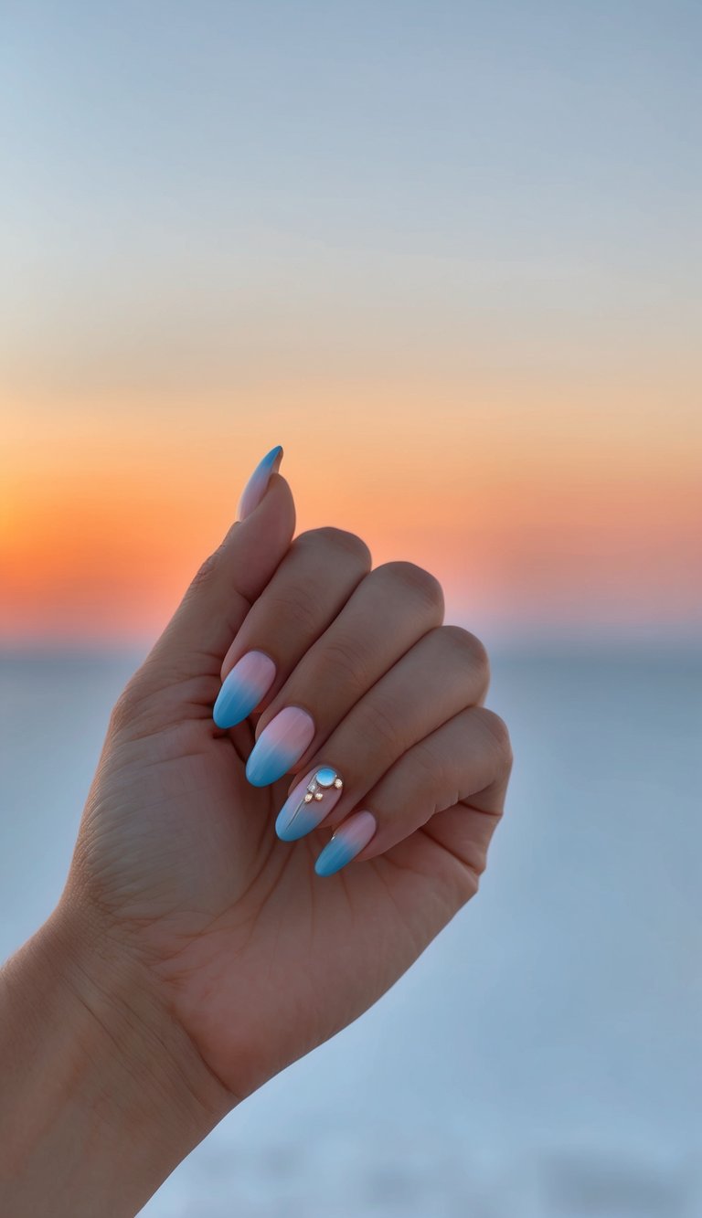 Close-up of fingers held against a warm sunset horizon showing a short nail art idea with pink-to-blue gradient polish and a small gemstone embellishment on one nail.