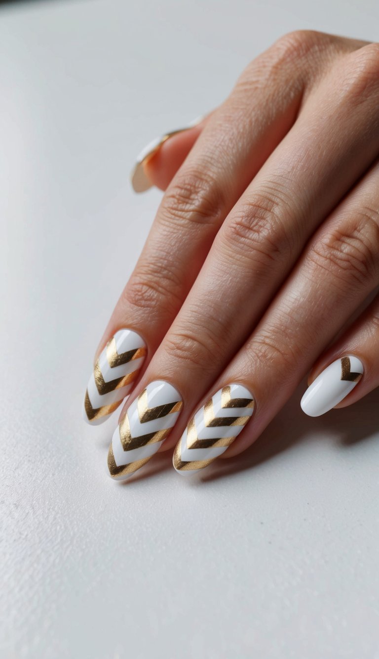 Hand resting on a smooth surface showing a white and gold nail art idea with glossy white almond nails painted with diagonal gold stripe patterns forming chevron designs.