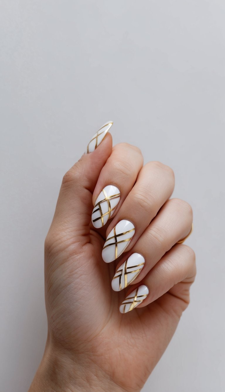 Hand with almond-shaped nails shown against a neutral background featuring a white and gold nail art idea with glossy white nails decorated with thin gold lines forming an intersecting grid pattern.