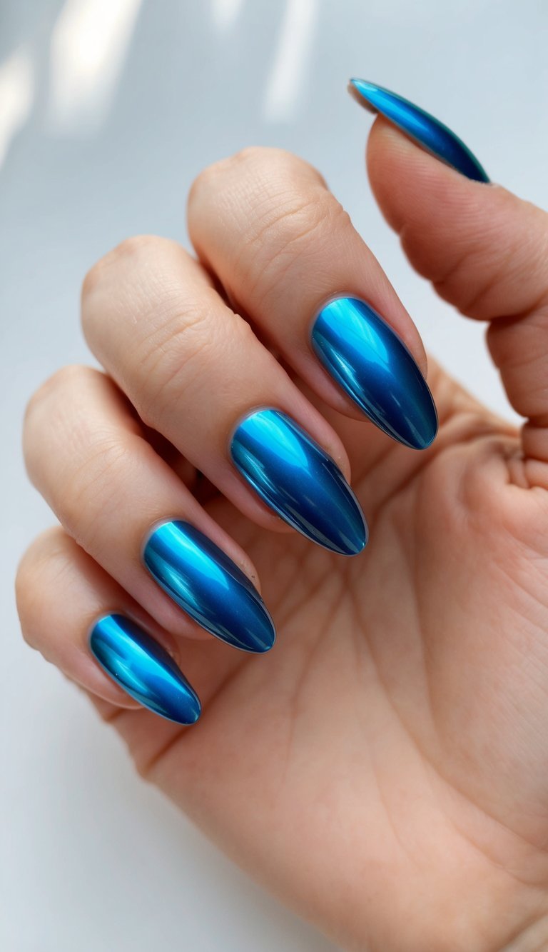 Manicured hand showing almond-shaped nails finished in cobalt blue chrome polish with mirror reflection, illustrating a chrome nail art idea photographed against a light background.
