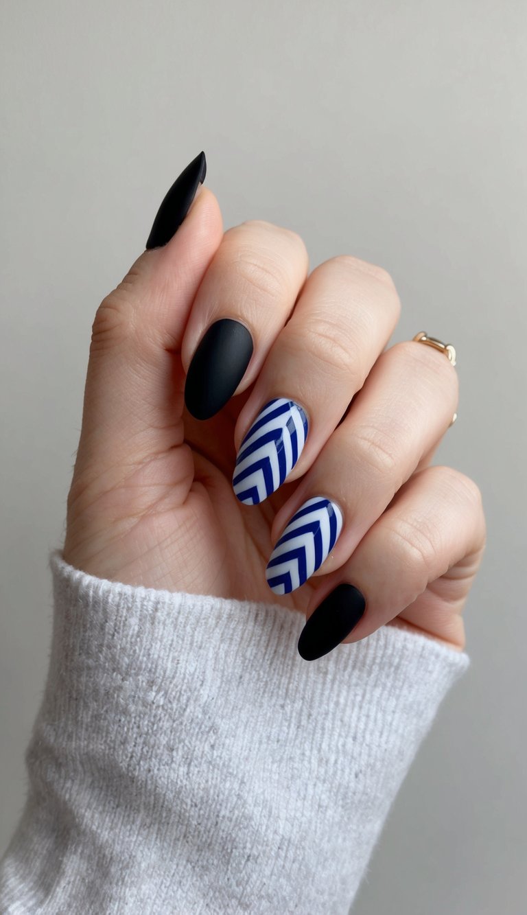 Fingers curled slightly while wearing a soft sweater, showing a black and blue nail art idea with matte black nails and bold cobalt chevron stripe nail art.