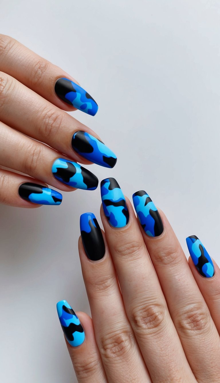 Close-up of both hands featuring a black and blue nail art idea with abstract blue camouflage patterns layered over matte black nails on long square-shaped tips.