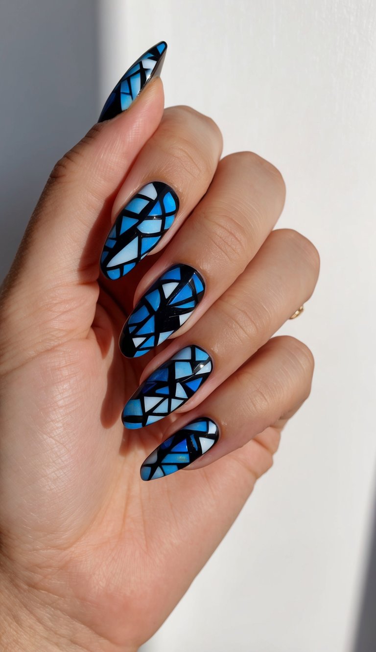Hand held near a softly lit wall showing a black and blue nail art idea with stained-glass style nail art made of cobalt, navy, and pale blue panels outlined in black.
