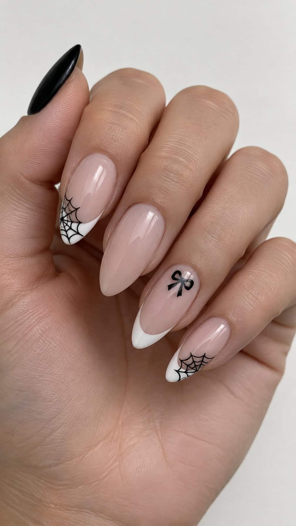 Almond-shaped nails featuring glossy nude polish, white French tips, black web designs, and small black bows