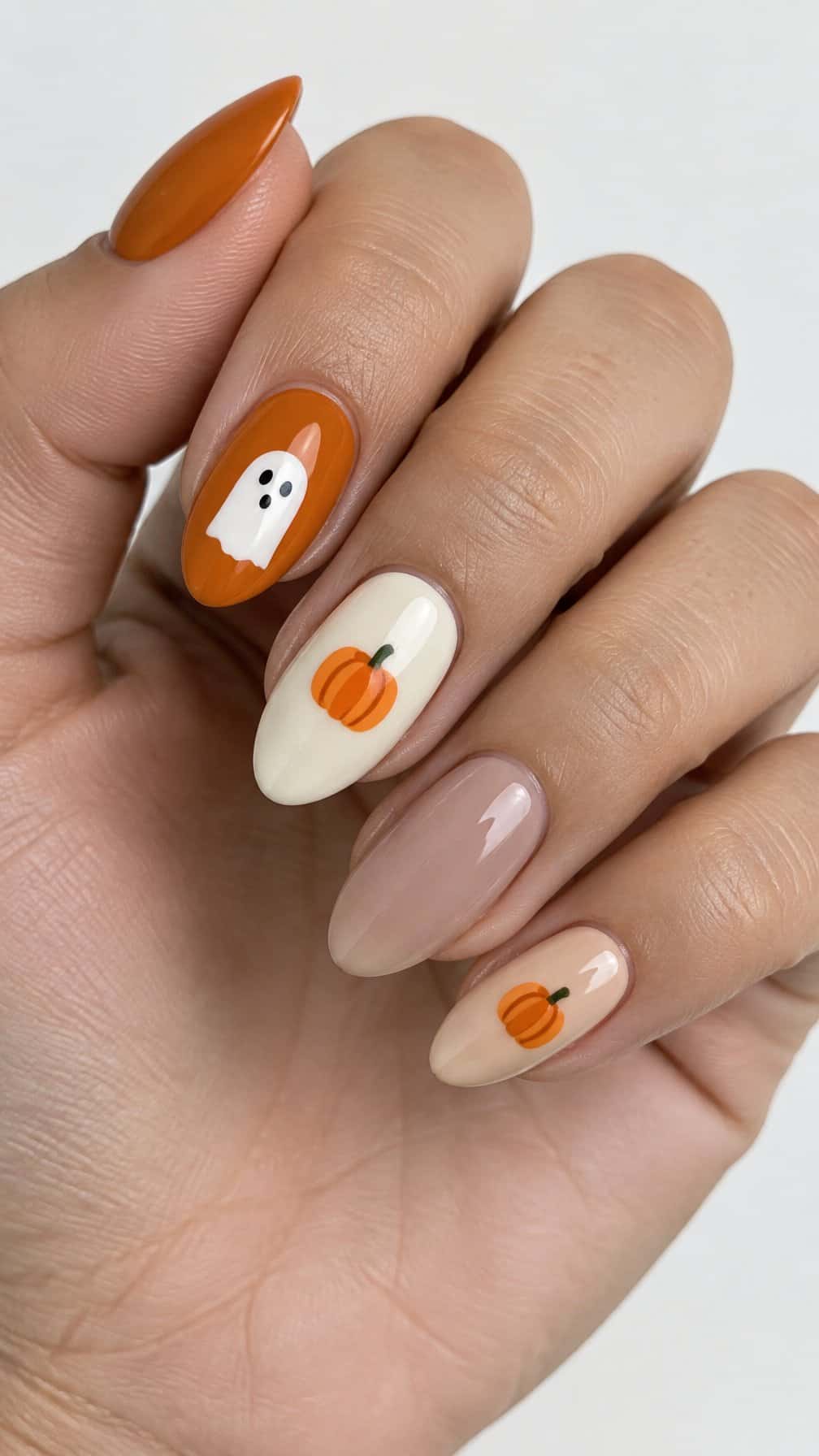 Glossy almond-shaped nails decorated with white ghosts, orange pumpkins, and solid autumn colors
