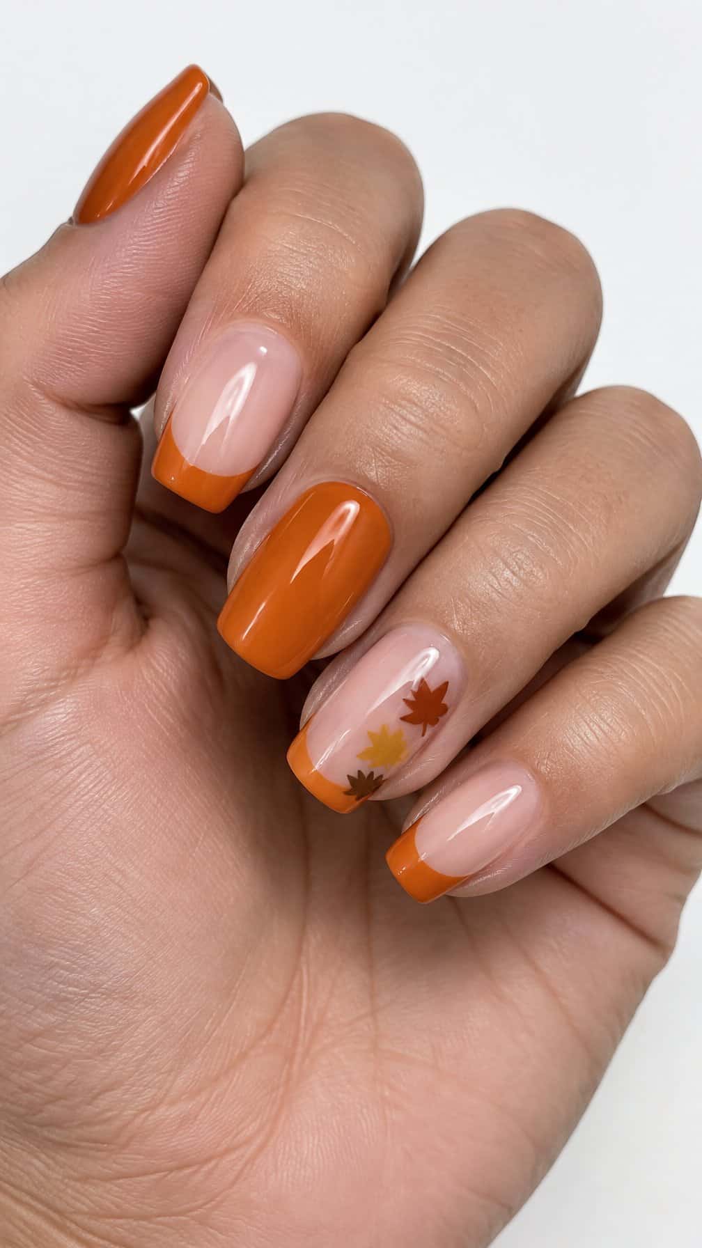 Glossy orange French-tip nails and tiny autumn leaf designs