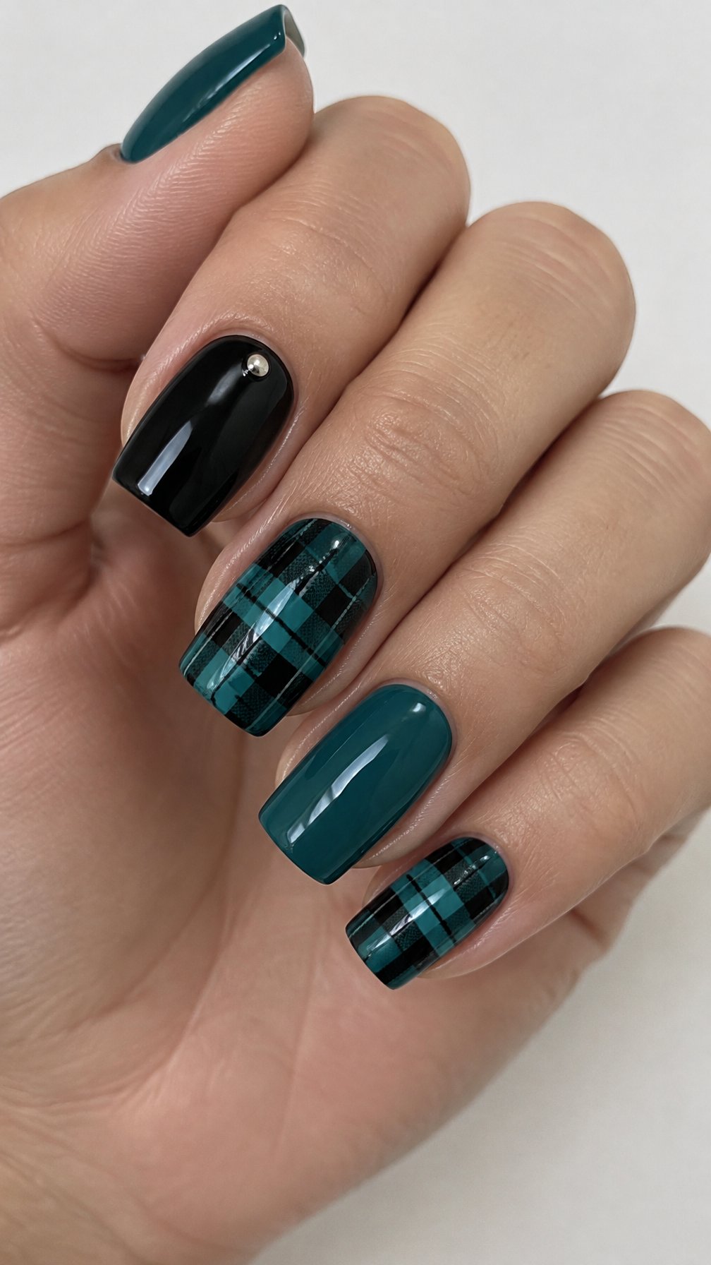 Glossy black and teal plaid nails, solid accent nails, and small metallic studs
