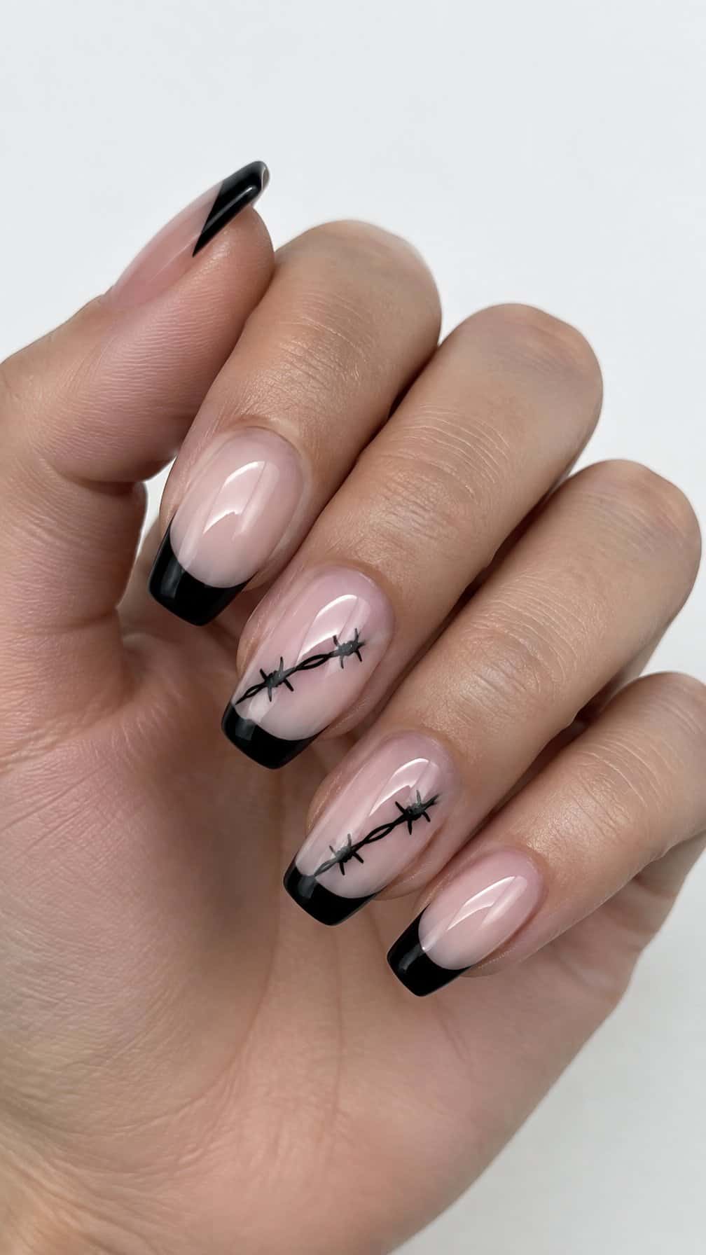 Glossy black French-tip nails and small barbed-wire designs on two accent nails