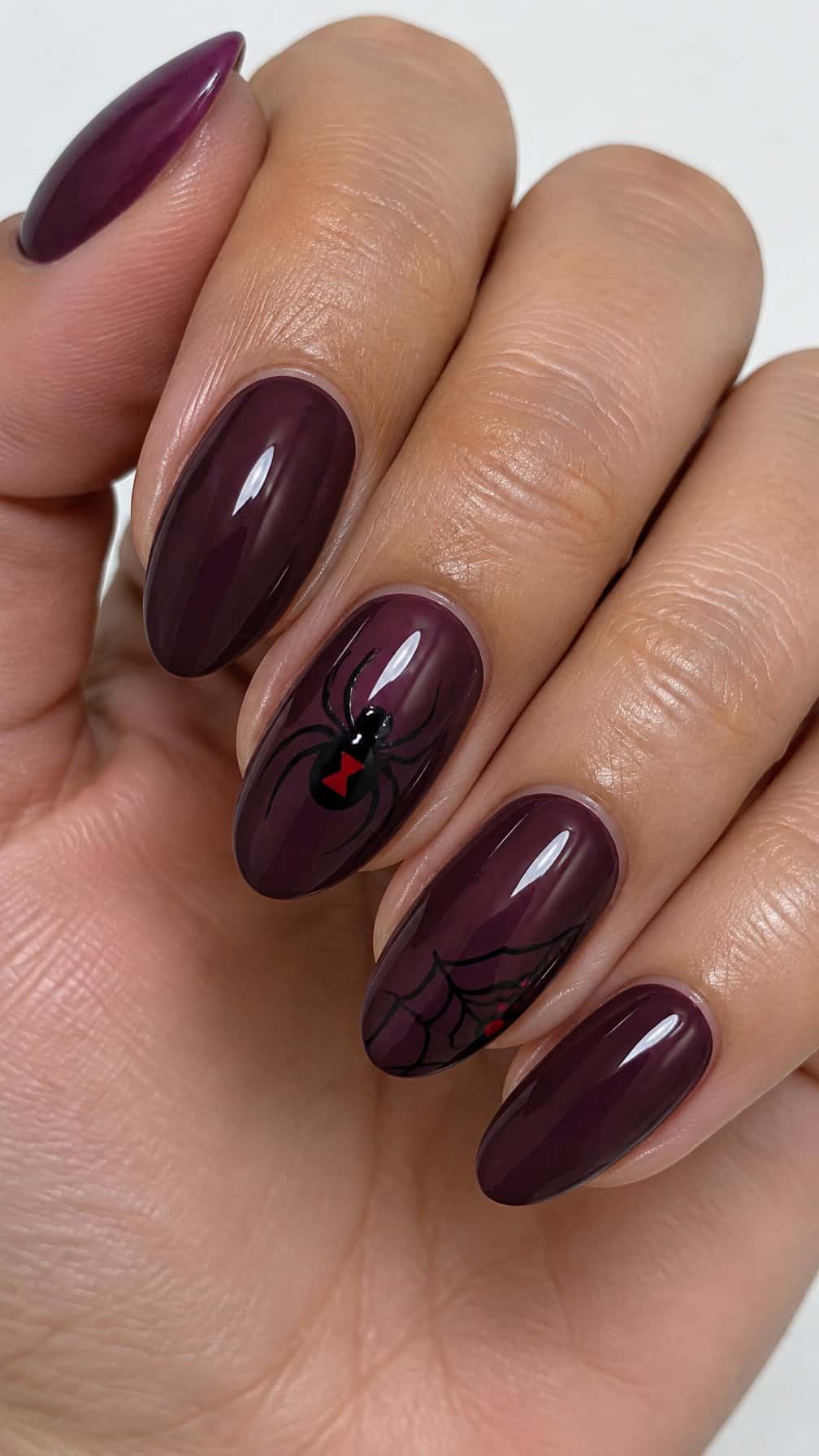 Glossy plum-purple nails featuring black widow spider designs on two accent nails