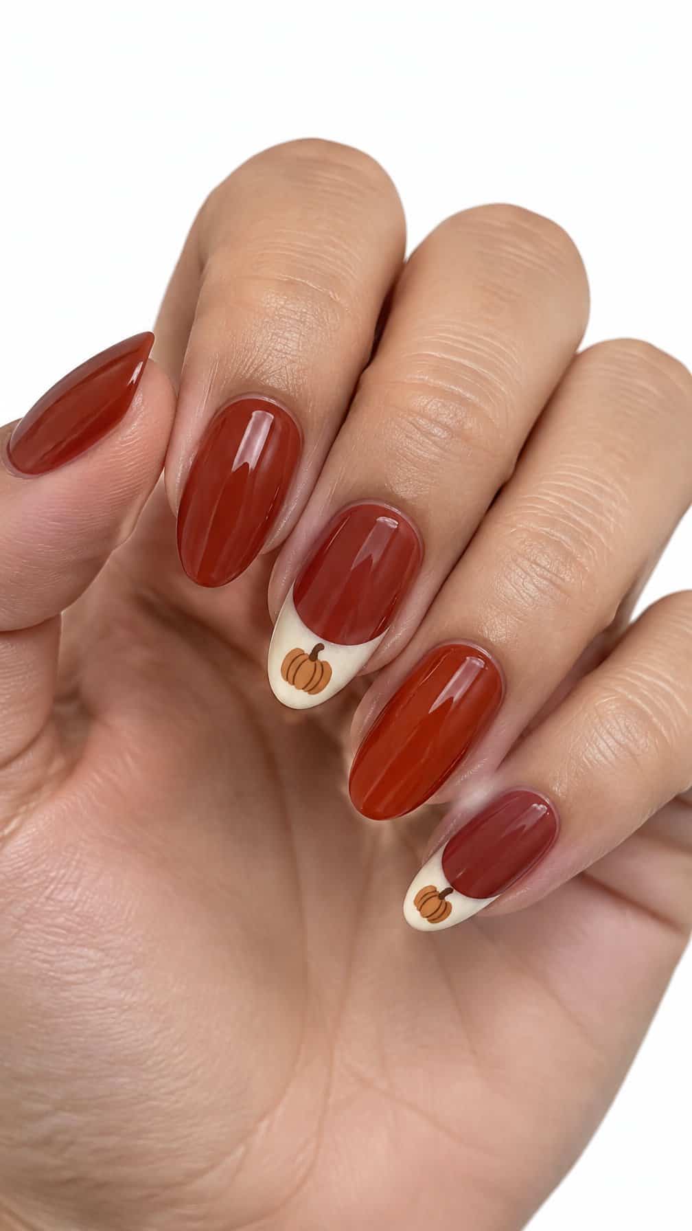 Glossy brick-red nails, cream French tips, and small pumpkin designs