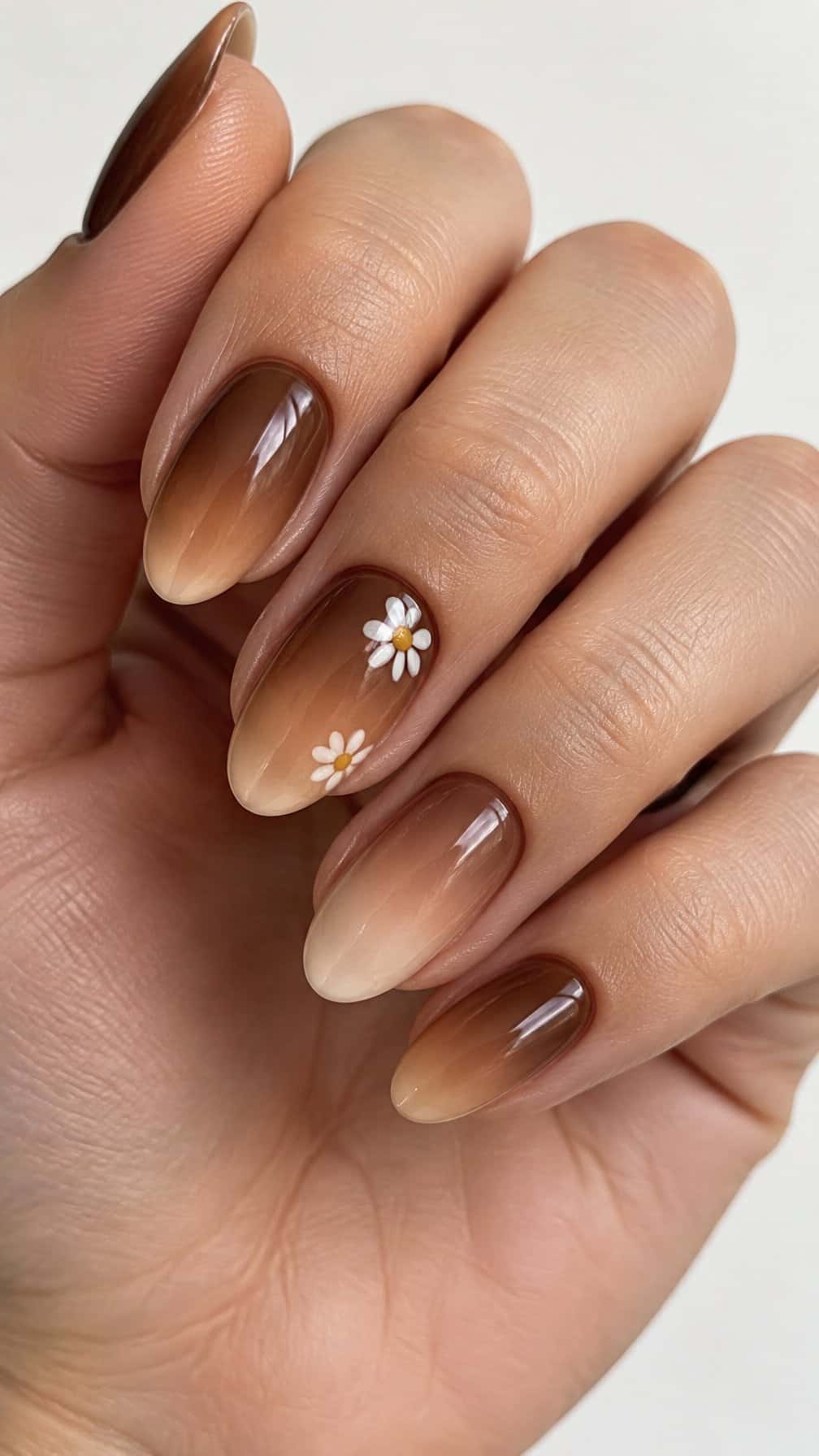 Glossy brown ombre nails, including small white daisy designs on two nails
